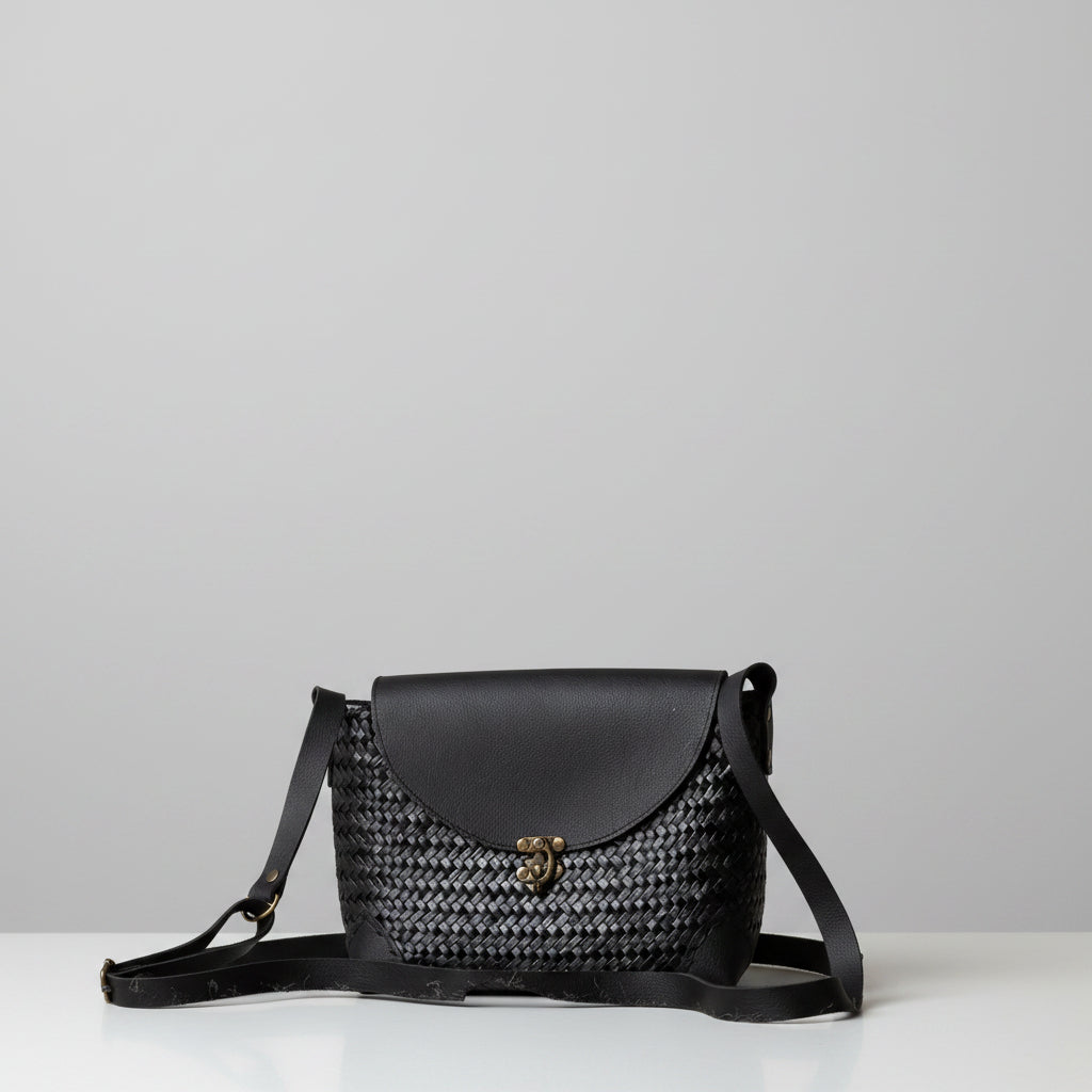 Black handbag with woven pattern on a wooden surface and rustic wooden wall background