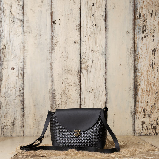Black handbag with woven pattern on a wooden surface and rustic wooden wall background